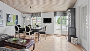 Un comedor con una mesa y sillas, un televisor montado en la pared y una cocina con refrigerador y armarios.