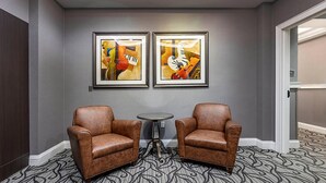 Un couloir avec deux fauteuils en cuir marron et une petite table ronde, et des tableaux abstraits accrochés au mur.