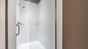 A modern bathroom with white tiles, a shower, and a glass partition.