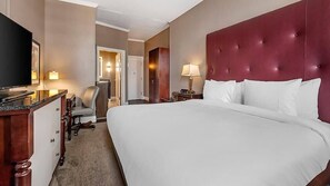 A hotel room with a large bed, a television, a desk, and a chair.
