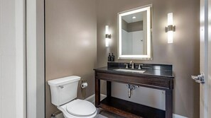 Ein Badezimmer mit Toilette, Waschbecken, Spiegel und Wandleuchten.