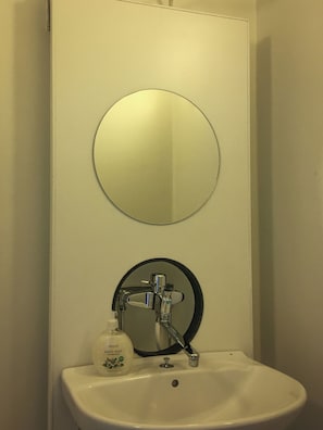 Un baño con lavamanos blanco, espejo y dispensador de jabón.