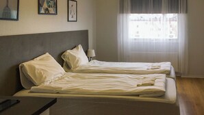 A hotel room with two beds, a nightstand, a lamp, and a window with sheer curtains.