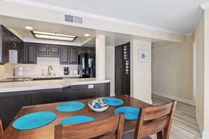 A modern kitchen with dark cabinets, a central island, and a dining area with a wooden table and blue placemats.