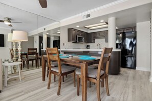 Eine moderne Küche mit dunklen Schränken, einem Edelstahl-Kühlschrank und einem Essbereich mit Holztischen und -stühlen.