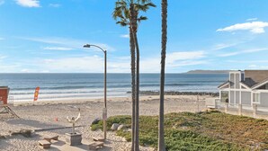 Blick auf einen Strand mit Palmen, einem Rettungsturm und einem Gebäude mit Balkon mit Meerblick.