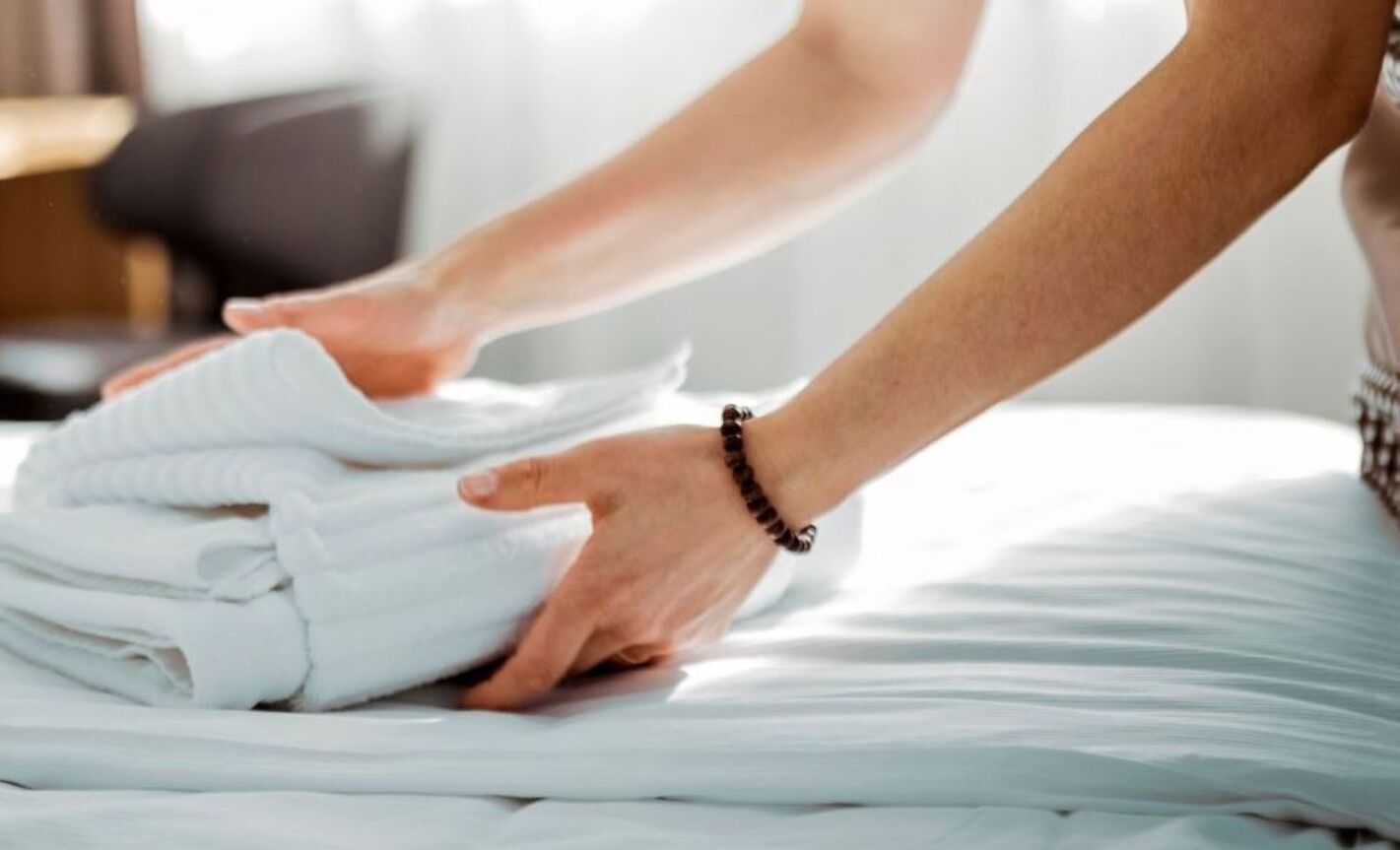 A person folding white linens on a bed.
