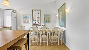 Un comedor con mesa de madera y sillas blancas, un refrigerador blanco y obras de arte enmarcadas en las paredes.