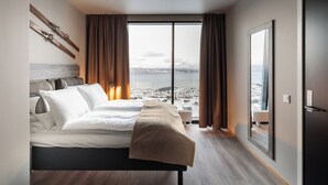 A modern hotel room with a large bed, a view of a snowy landscape, and a sliding glass door.