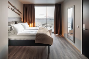 A modern hotel room with a large bed, a view of a snowy landscape, and a sliding glass door. - Basecamp Narvik (Narvik)