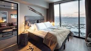 A modern bedroom with a large bed, a view of a cityscape, and a cozy seating area with a sofa and coffee table.