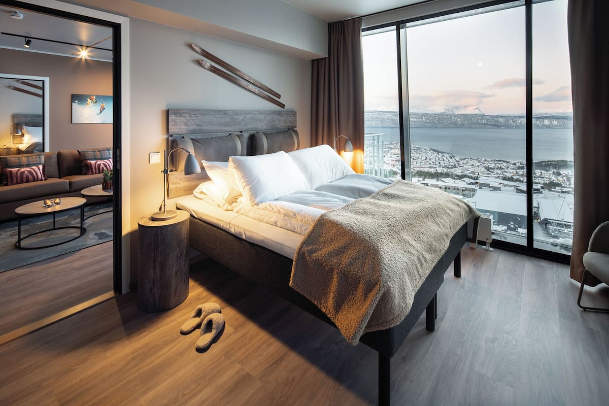 A modern bedroom with a large bed, a view of a cityscape, and a cozy seating area with a sofa and coffee table.