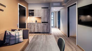 A modern hotel room with a sofa, a small table, a kitchen area, and a view of the outdoors.