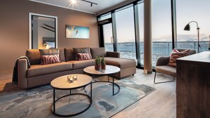 Un salon moderne avec un canapé, deux tables basses et une vue sur le paysage urbain, visible à travers de grandes fenêtres.