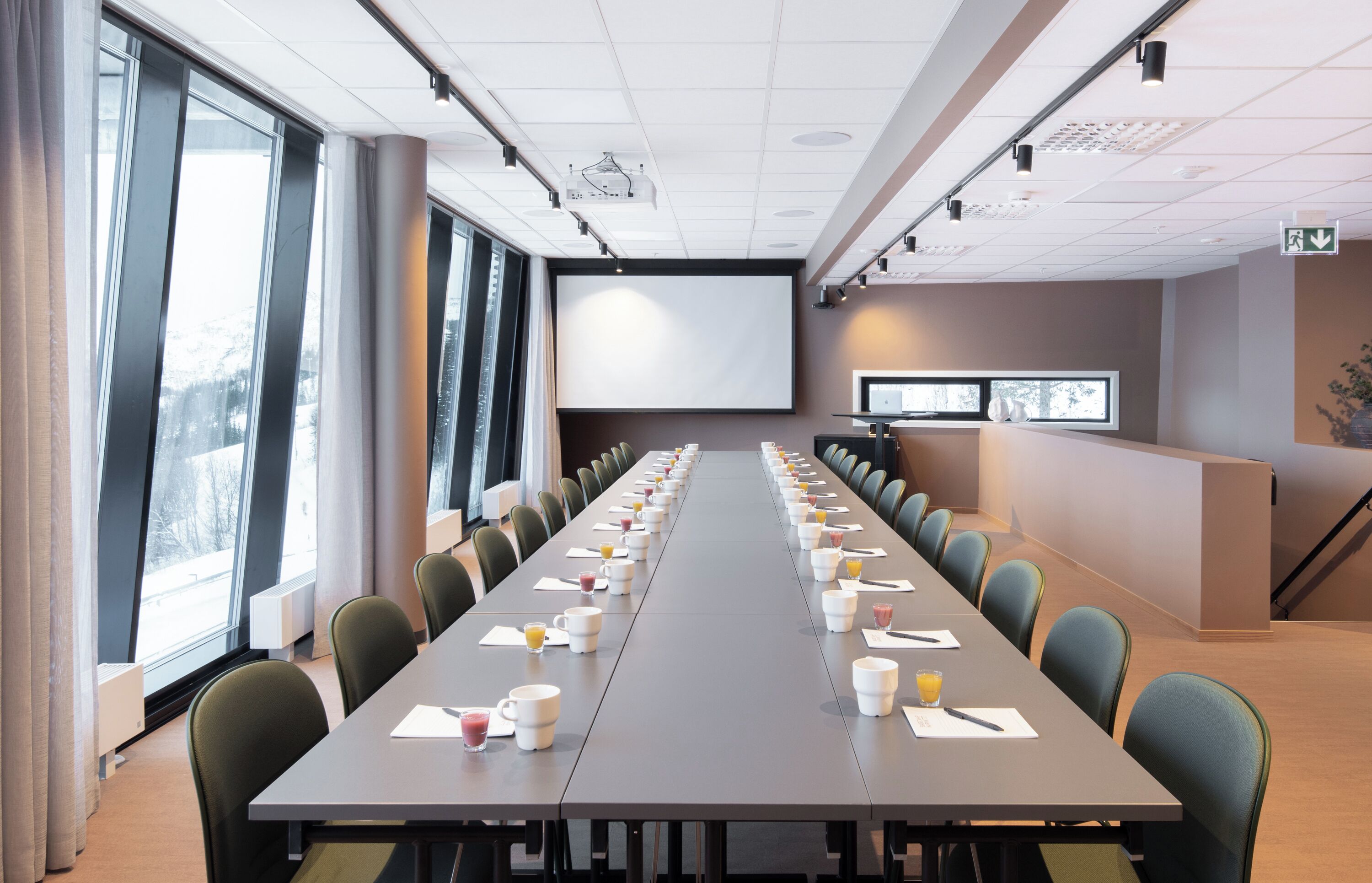 Un salón de conferencias con una larga mesa, sillas, una pantalla de proyector y una mesa de recepción.