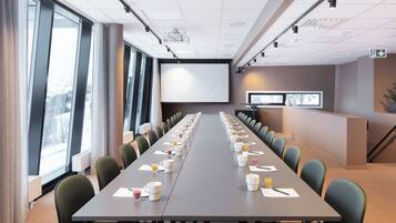Un salón de conferencias con una larga mesa, sillas, una pantalla de proyector y una mesa de recepción.