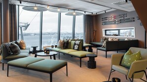 A modern lounge area with seating arrangements, a ski rack, and a large window offering a view of a snowy landscape.