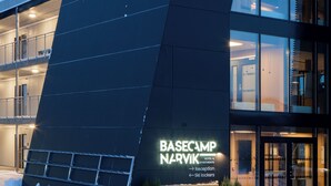 A modern building with a sign reading "BASECAMP NARVIK HOTEL & APARTMENTS" and an arrow pointing to the reception.