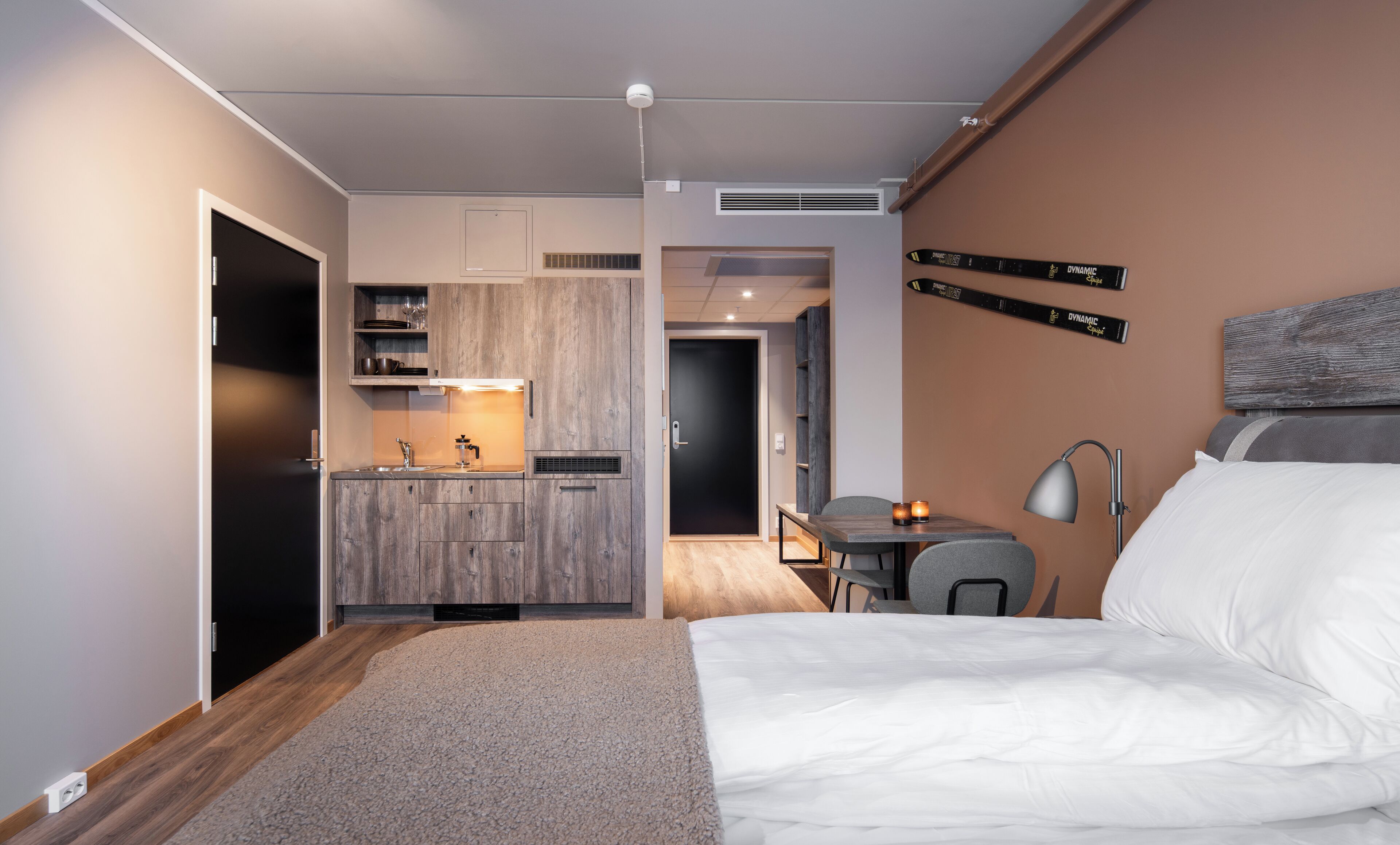 A modern hotel room with a kitchenette, a dining area, and a bed.
