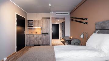 A modern hotel room with a kitchenette, a dining area, and a bed.