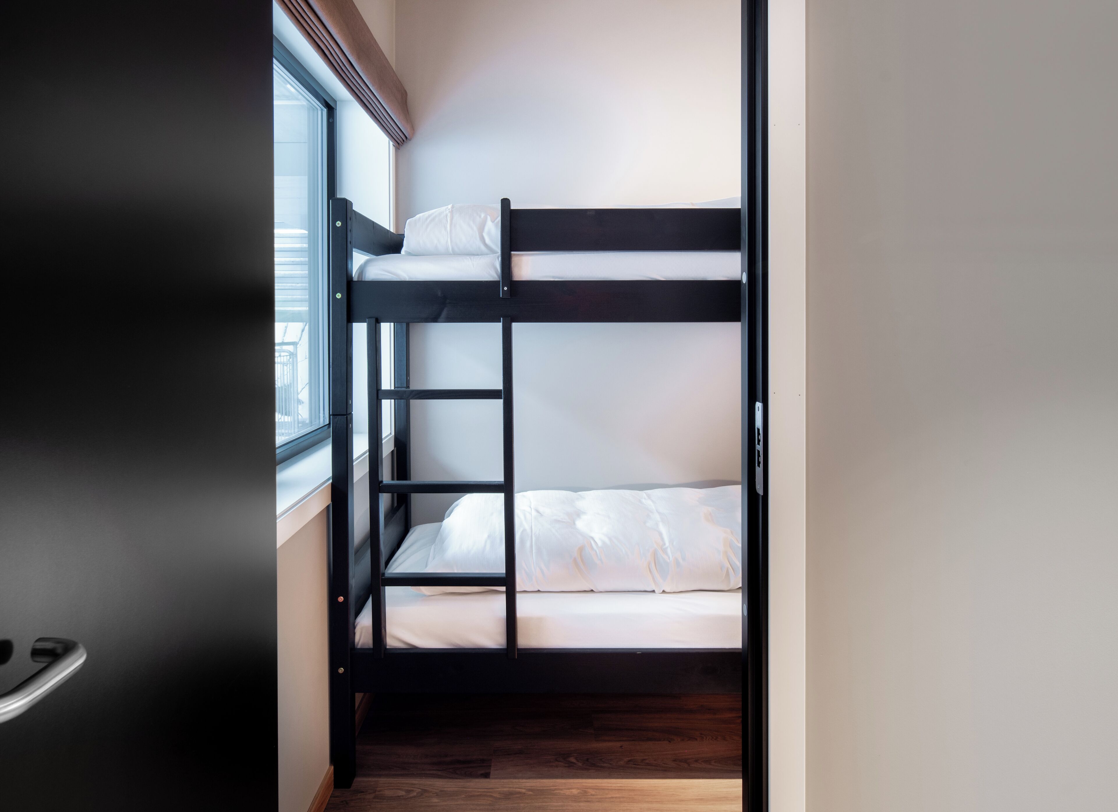 A bunk bed in a room with a window and wooden flooring.
