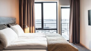 Une chambre d’hôtel avec un grand lit, une vue sur un paysage enneigé par la fenêtre et un téléviseur fixé au mur.