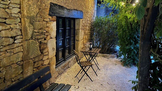 Un bâtiment en pierre avec une fenêtre, un banc et une table entourée de chaises.