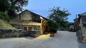 Un bâtiment rustique en pierre, avec une allée de gravier, une porte en bois et un petit porche.