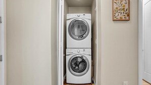 A laundry room with two stacked washing machines and a framed floral artwork on the wall. - Poolside Paradise 3 | 3BR Legacy Villa (La Quinta)