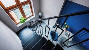 Una escalera con barandilla negra, una puerta azul y un ventanal con planta en la plataforma.