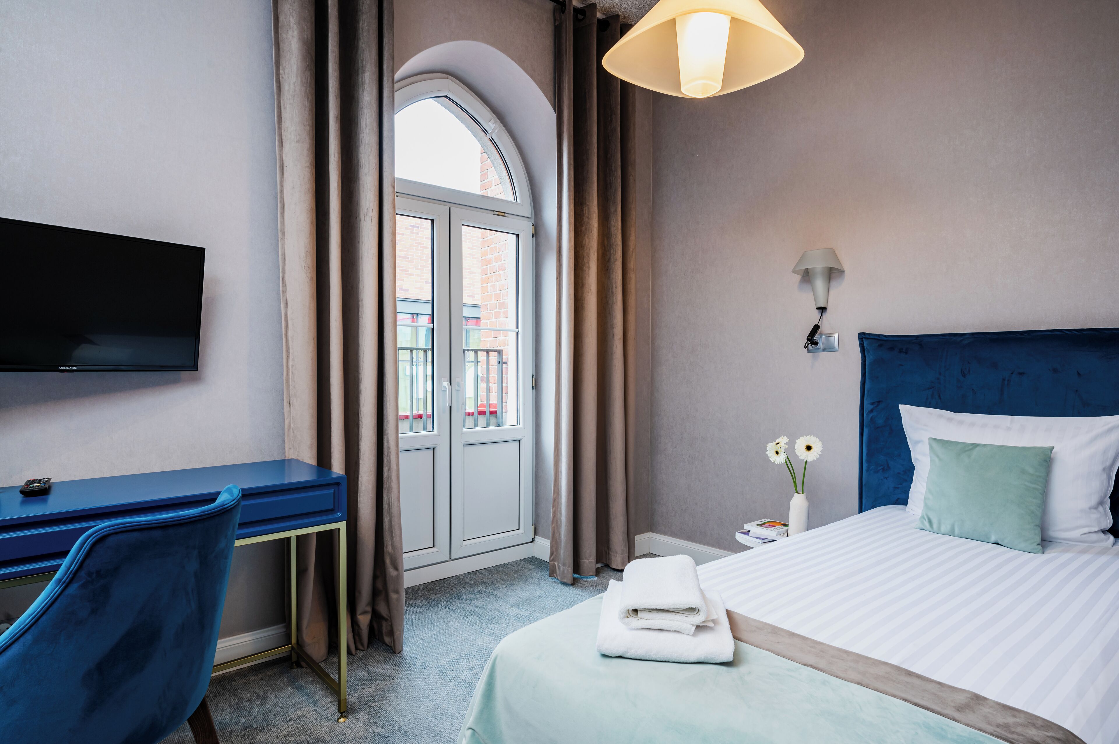 A hotel room with a bed, a desk, a chair, a TV, and a window with curtains.