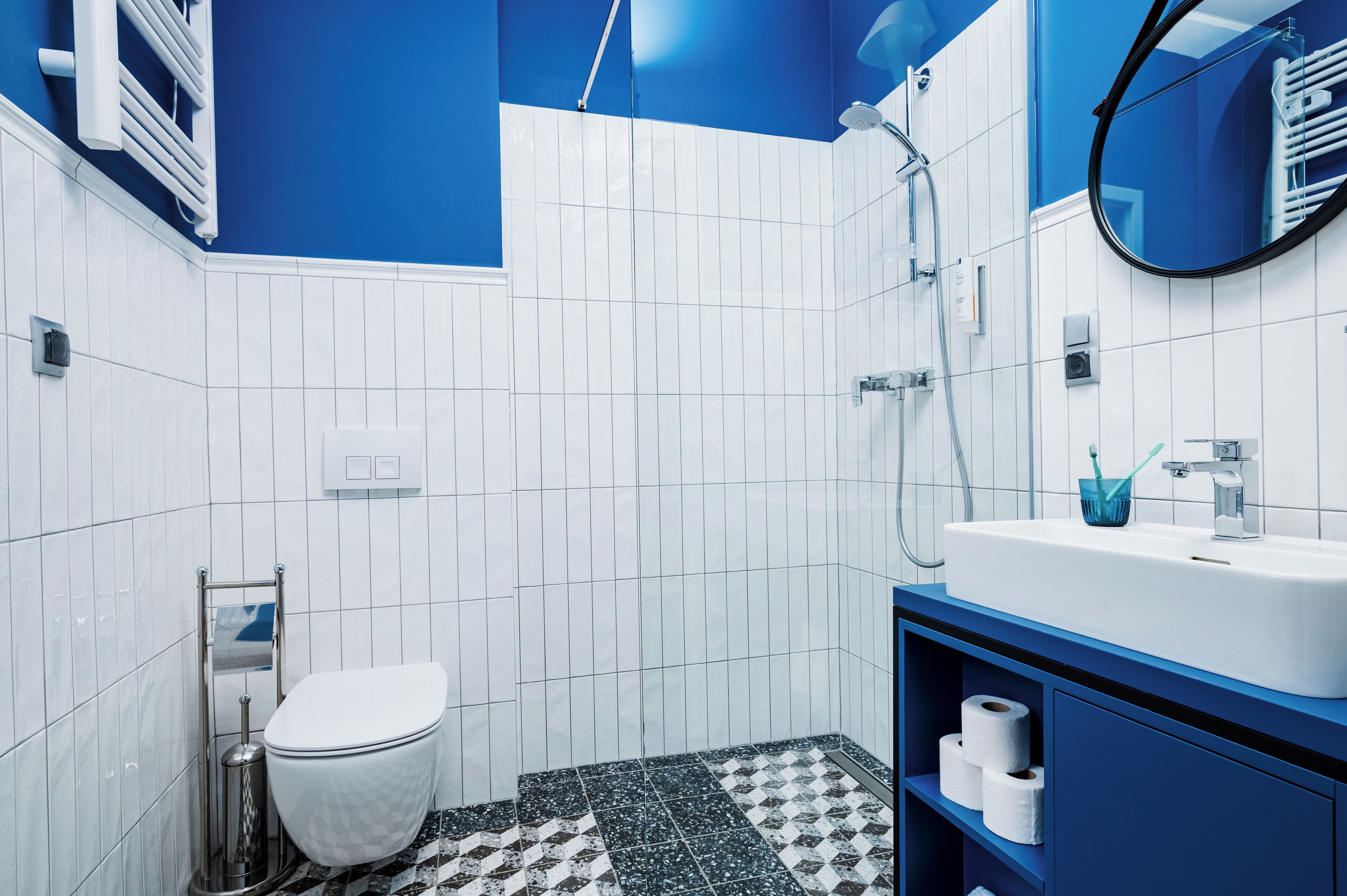 A modern bathroom with white and blue tiles, a white toilet, a sink with a blue cup, and a shower.
