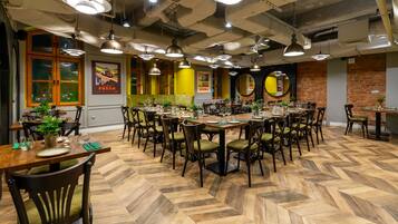 Un restaurante con varias mesas dispuestas para comer, suelo de madera con diseño de espiga y lámparas colgantes.