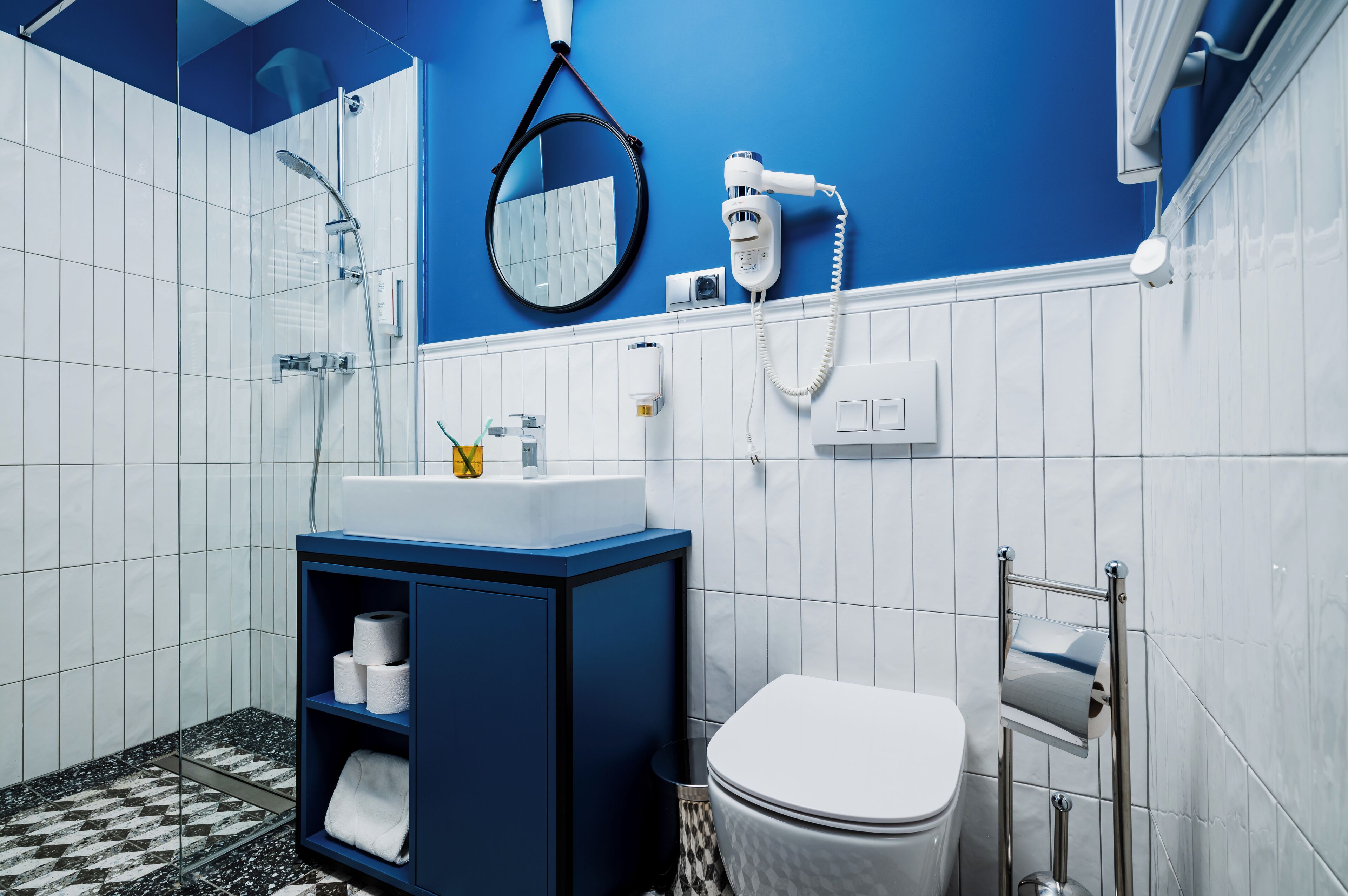 A modern bathroom with a blue accent wall, a white sink, a mirror, a hairdryer, and a toilet.