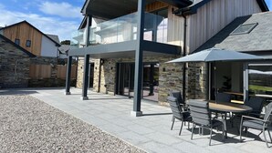 A modern two-story house with a stone facade, a glass conservatory, and an outdoor seating area with a table and chairs. - Luxury Home in the heart of Cornwall's Seven Bays area, close to Padstow  (PADSTOW)