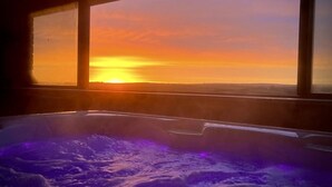 A room with a large window overlooking a sunset, a hot tub, and a view of the landscape. - Luxury Home in the heart of Cornwall's Seven Bays area, close to Padstow  (PADSTOW)
