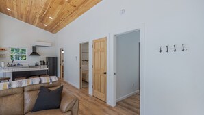 A modern kitchen with a central island, wooden ceiling, and a dining area with a striped tablecloth. - Black Haven Tiny Home (Surry)