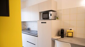 Una cucina con mobili bianchi, un forno a microonde, una macchina da caffè e una piccola pianta sul piano di lavoro.