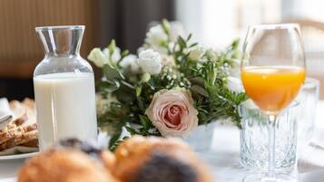 Um cenário de café da manhã com um garrafa de leite, um copo de suco de laranja, doces e um arranjo floral.