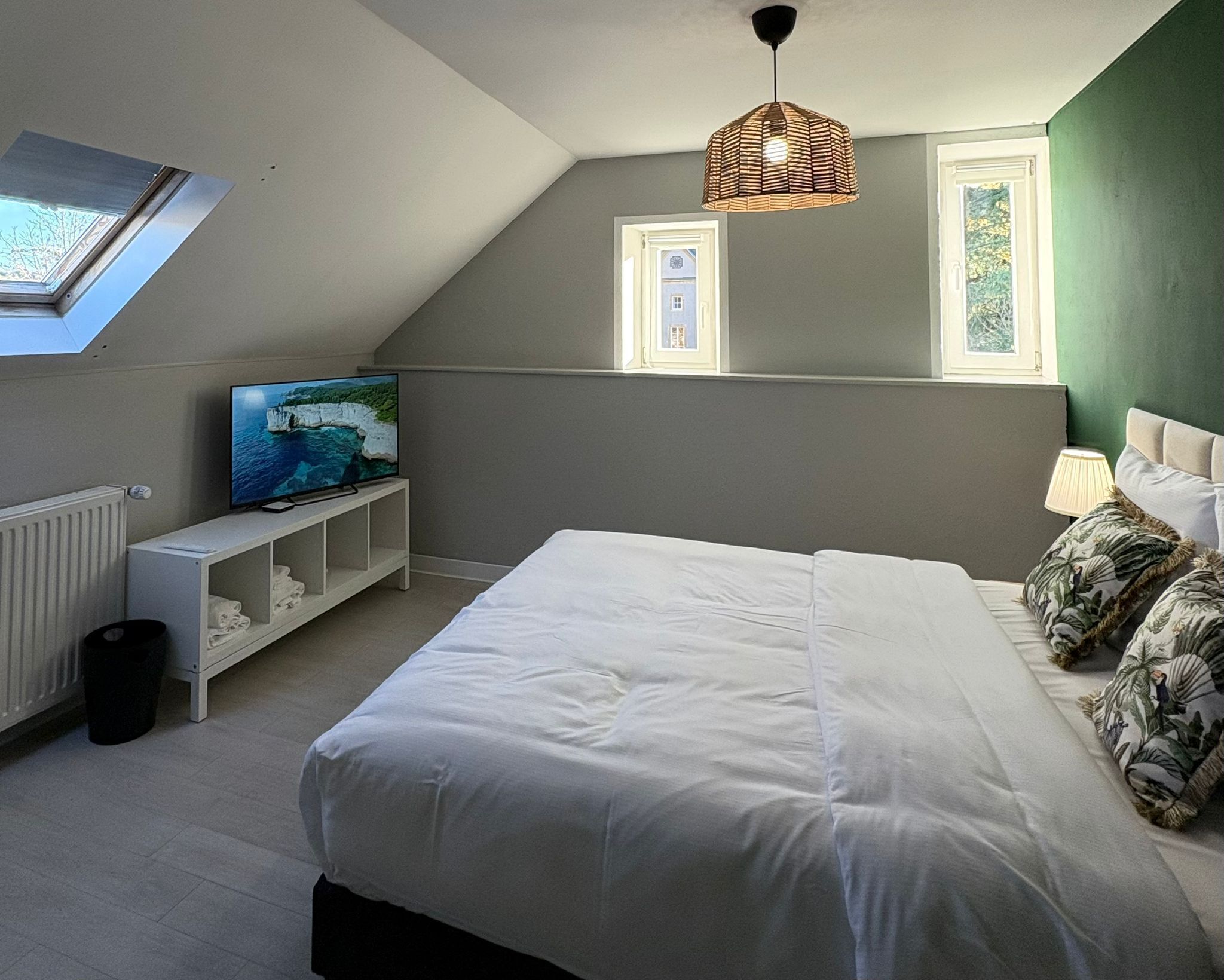 Een slaapkamer met een bed, een televisie op een standaard, een raam en een plafondlamp.