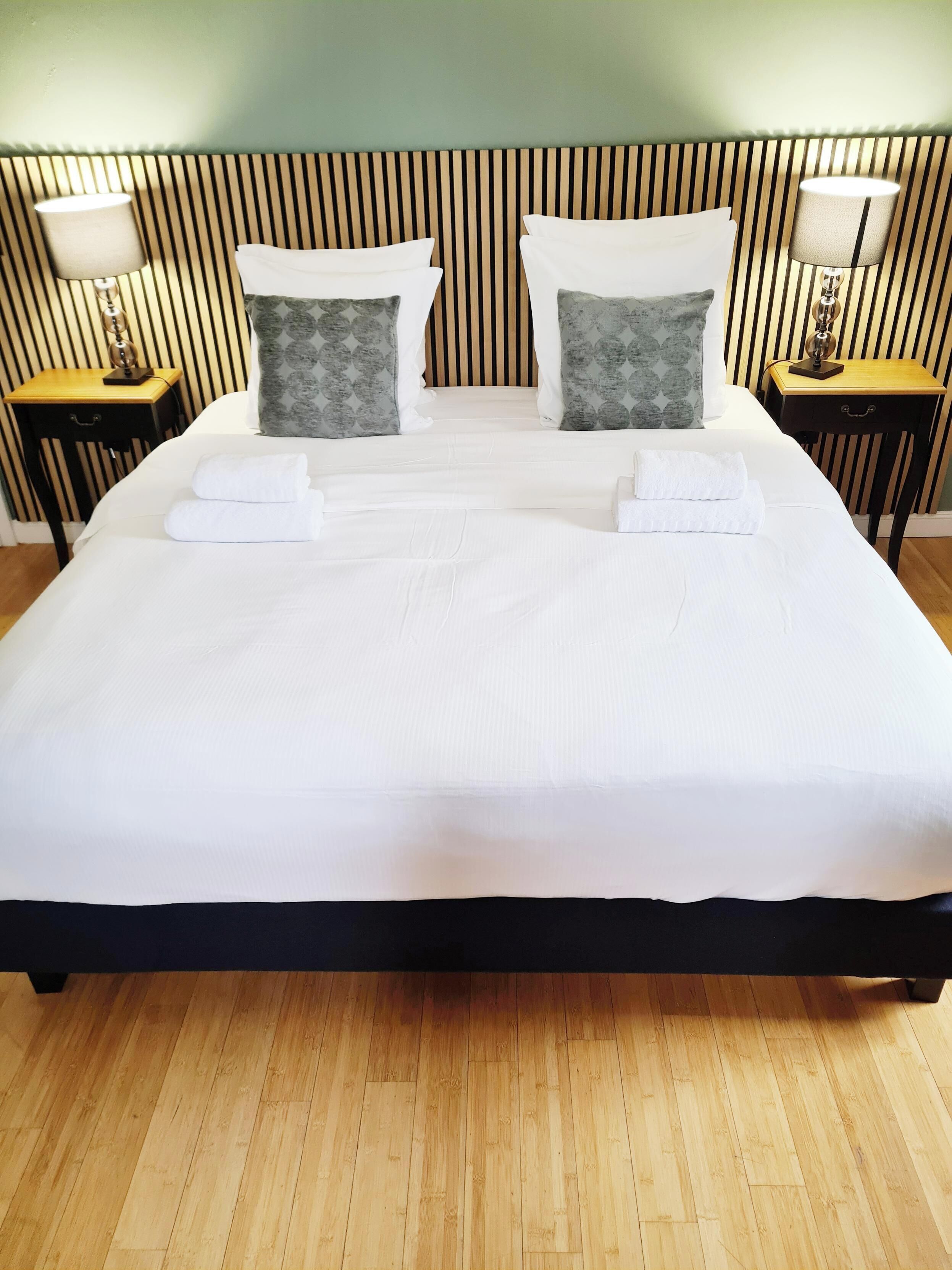 A neatly made bed with white linens and towels, two pillows, and a headboard with vertical stripes.