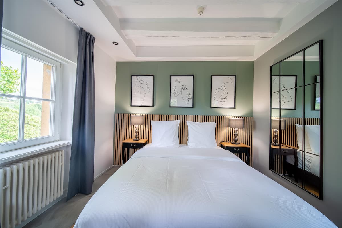 A hotel room with a large bed, two bedside tables with lamps, a large mirror, and three framed artworks on the wall.
