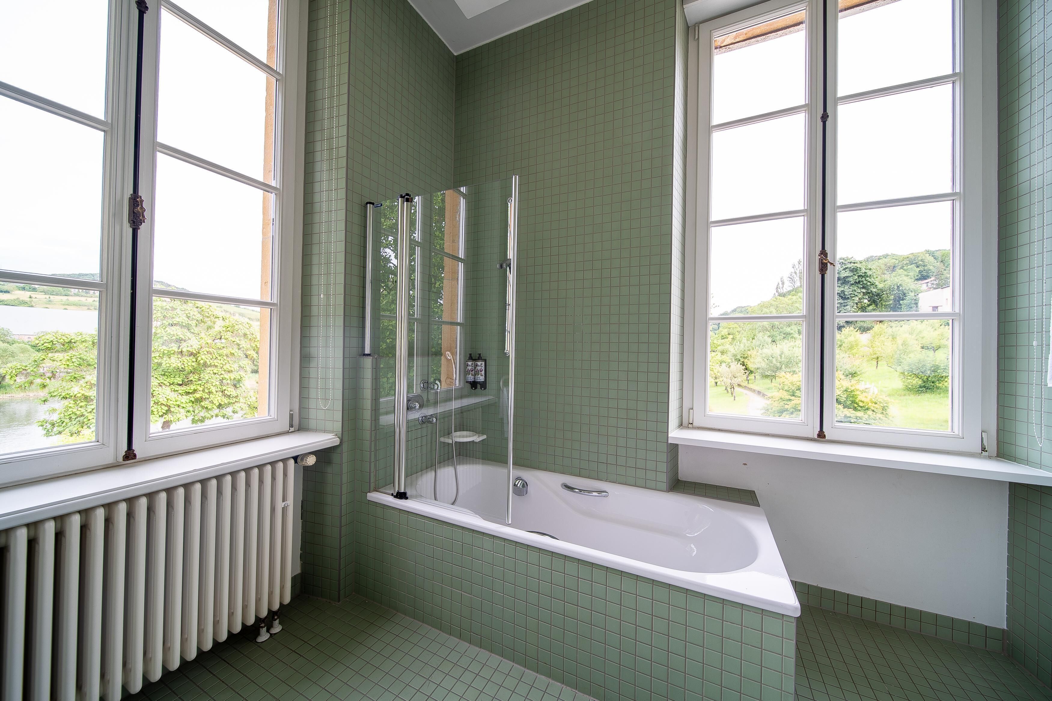 A bathroom with a bathtub, a shower enclosure, and large windows offering a view of greenery.