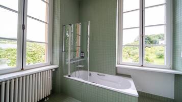 A bathroom with a bathtub, a shower enclosure, and large windows offering a view of greenery.