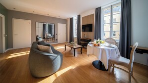 Un soggiorno moderno con un ampio pouf, un tavolo da pranzo per due persone e una TV a parete.