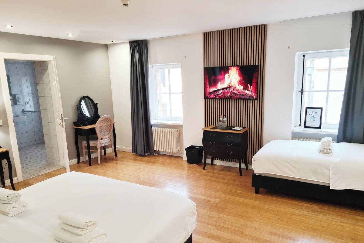 A hotel room with two beds, a TV, a desk with a chair, and a view of a fire.