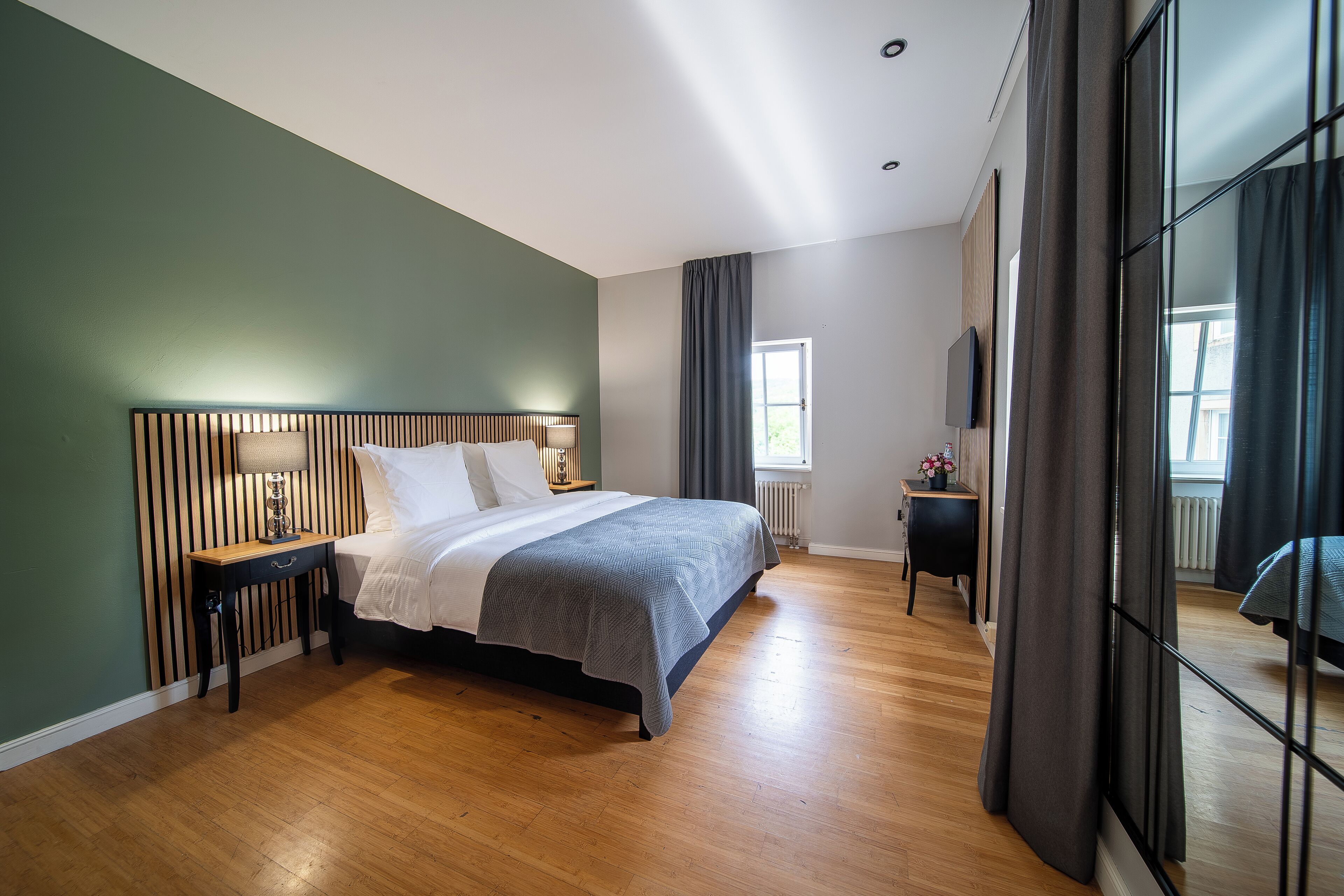 Una camera da letto moderna con una testiera in legno, un letto con lenzuola bianche, un comodino con una lampada e vista sull'esterno attraverso una finestra.