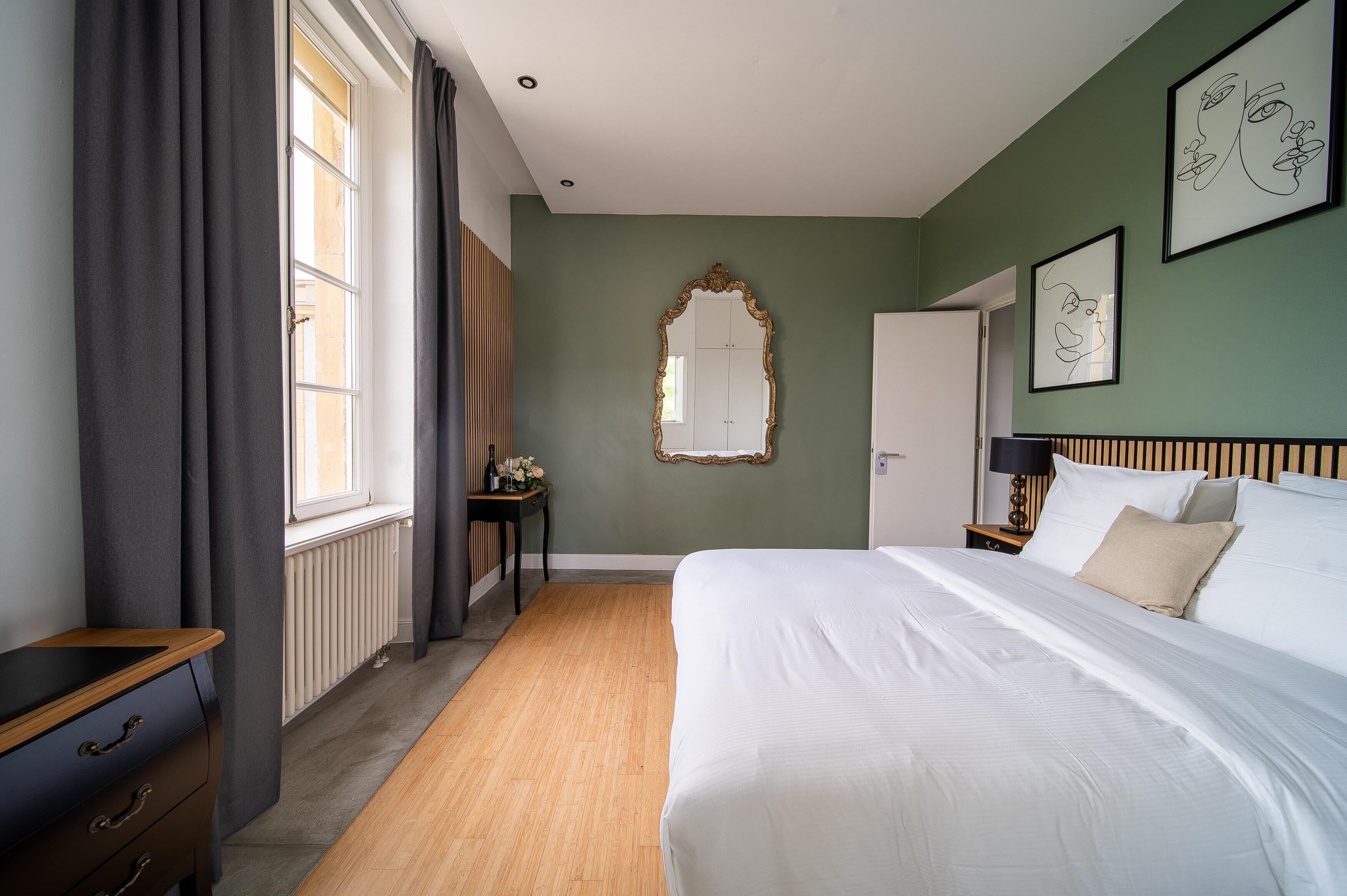 Un dormitorio ordenado con una cama grande, un tocador, una mesita de noche, un espejo y obras de arte enmarcadas en la pared.
