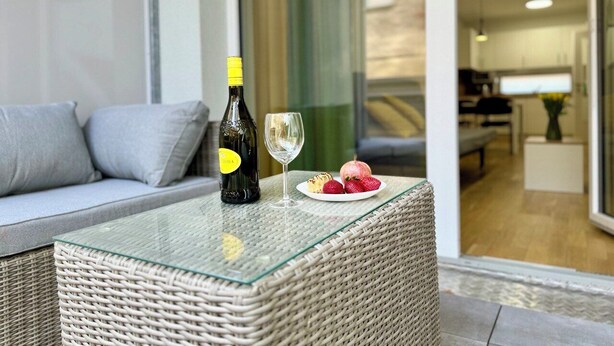 Una sala moderna con una mesa de centro de vidrio, una botella de vino y un plato de fruta.