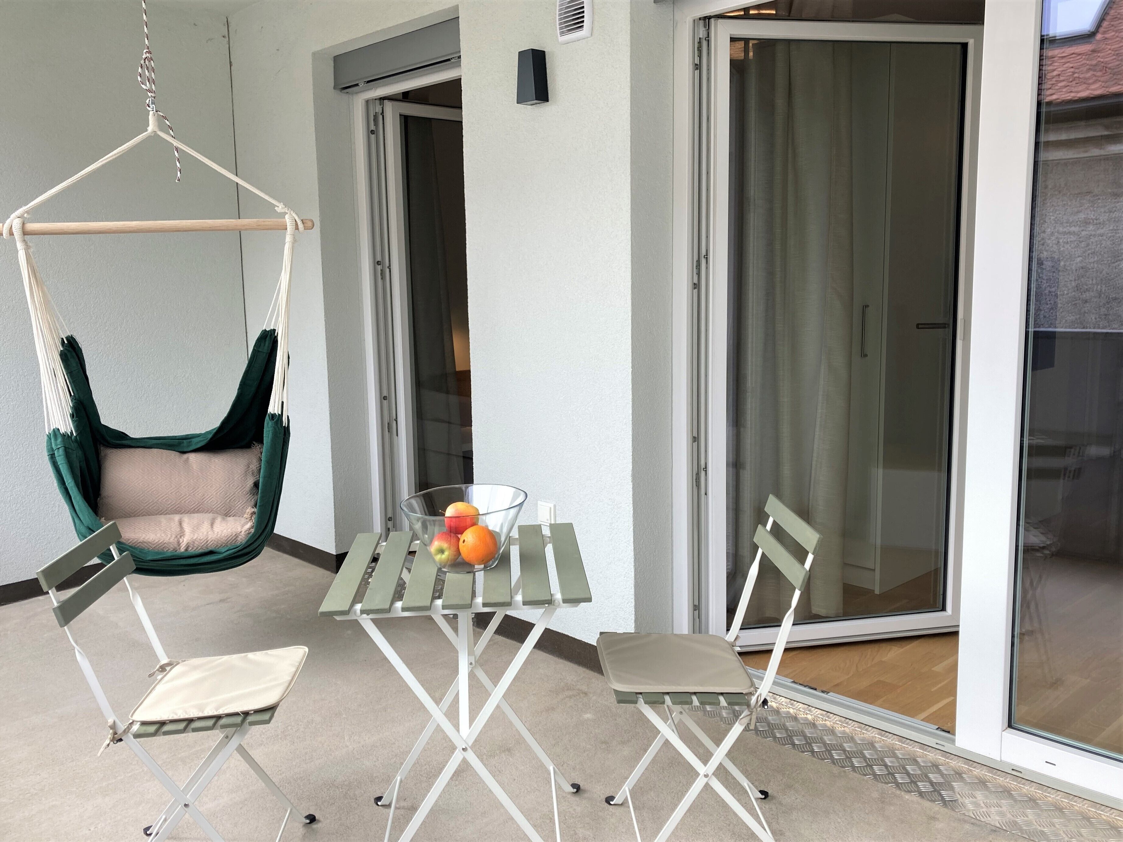 A balcony with a hanging chair, a table with chairs, and a fruit bowl.